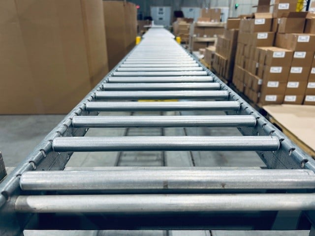 Roller conveyor running past labeled cartons stacked on pallets in KSP's kitting area