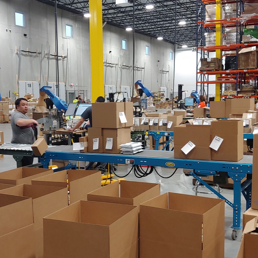 Packing stations and conveyor beside numbered pallet racking in a fulfillment warehouse